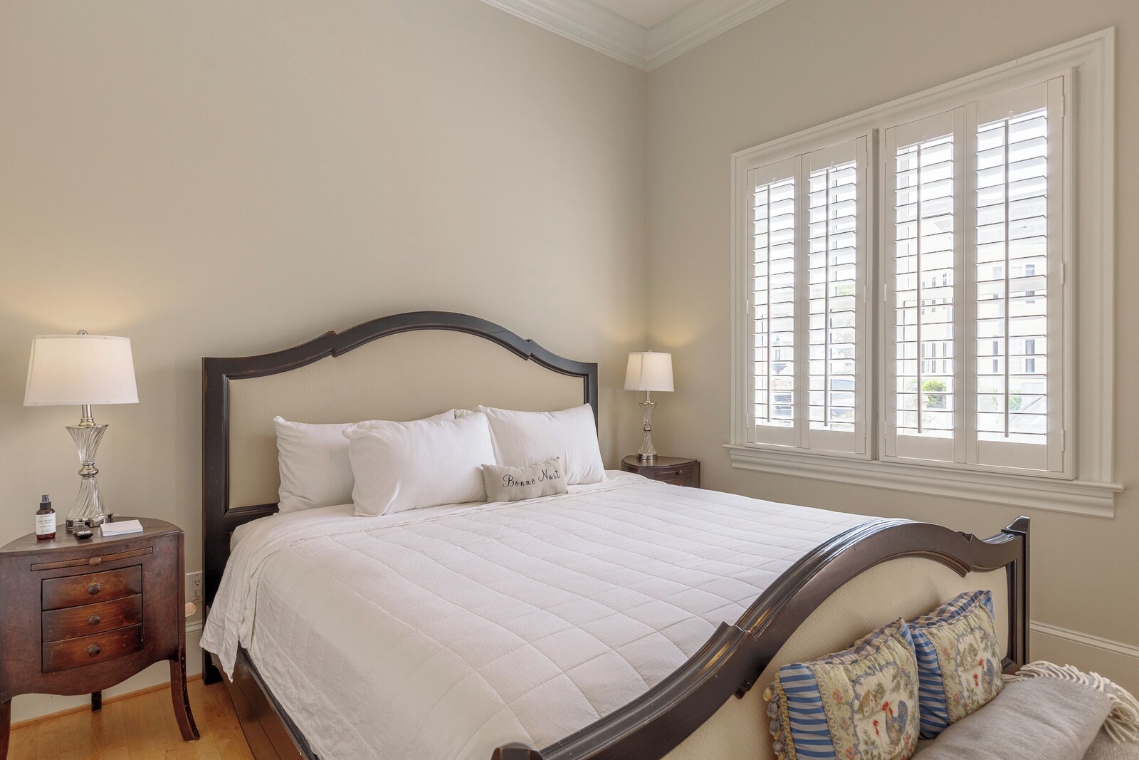 Guest bedroom with a dark wood sleigh bed, white quilted bedding, two lamps on wooden nightstands and a large shuttered window